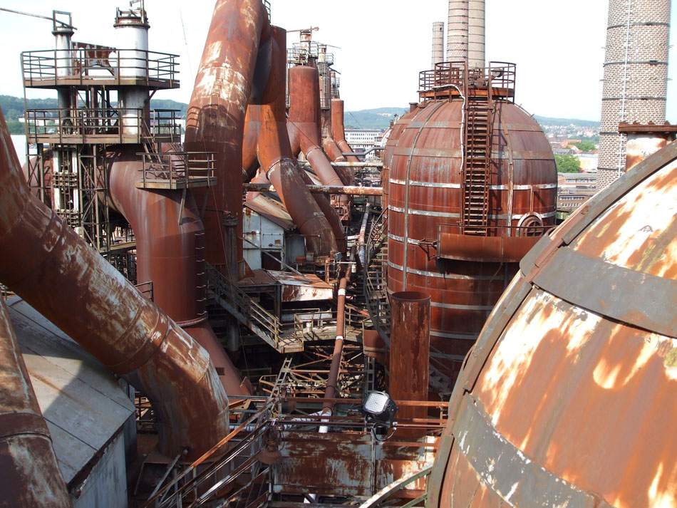 Rostrote Industrieanlage mit Kesseln über einer Stadtsilhouette