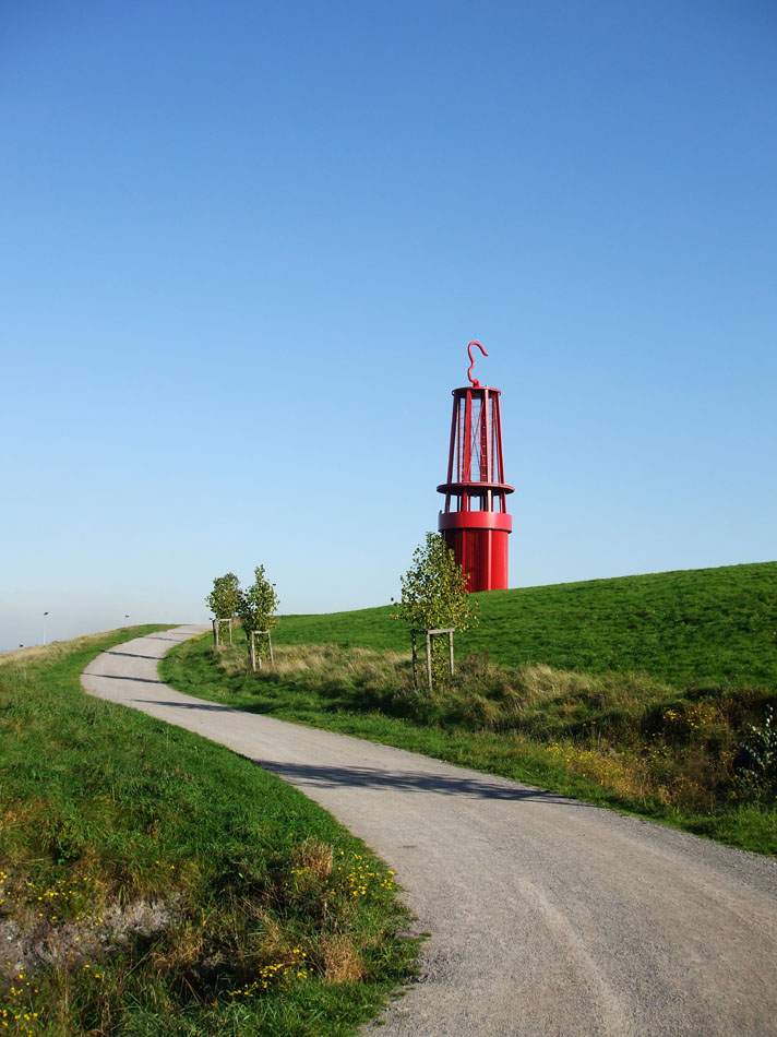 Rote Skulptur in Form einer überdimensionalen Grubenlampe auf einer begrünten Halde