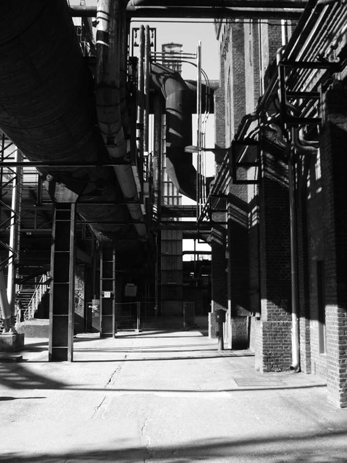 Gasse zwischen Industriebauten mit Rohrleitungen, Schwarz-Weiß