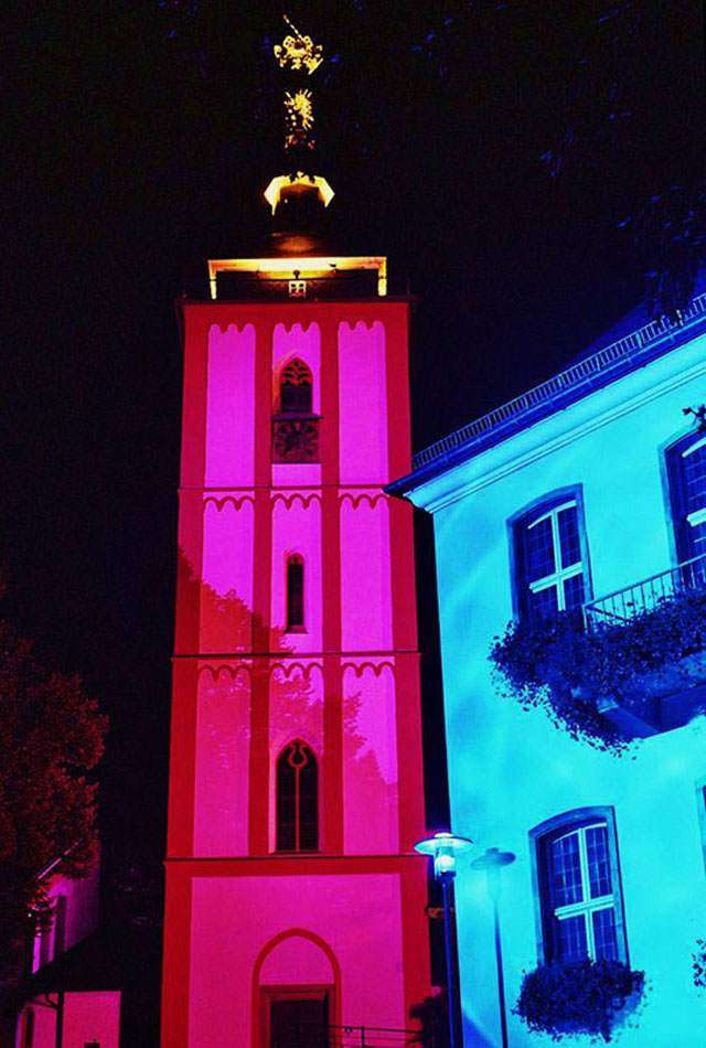 Illuminierte Nikolaikirche Siegen in Magenta neben blau angestrahltem Nachbargebäude
