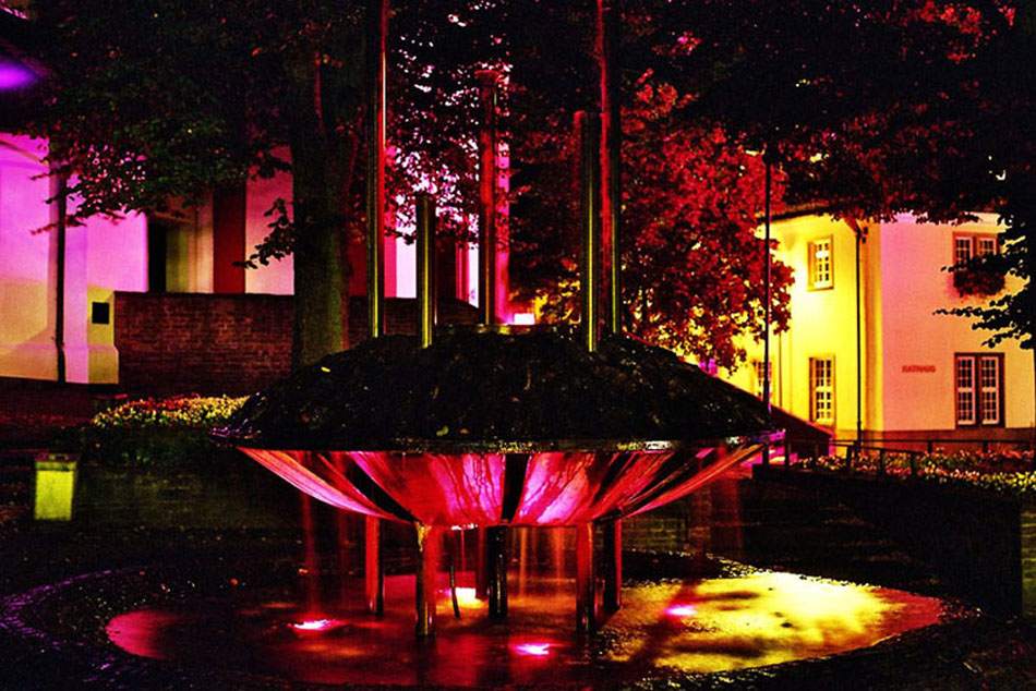 Historisches Gebäudeensemble mehrfarbig illuminiert, beleuchteter Brunnen im Vordergrund